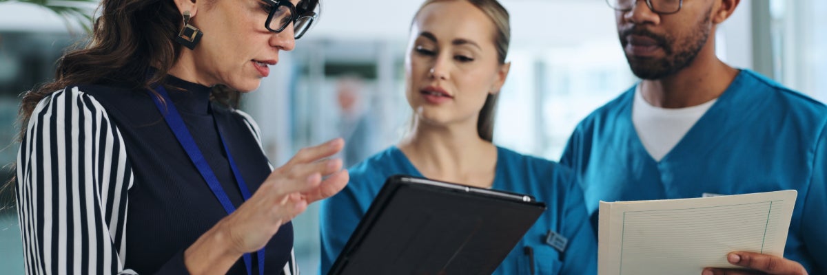 Three People looking at a tablet, and a man holding a piece of paper.