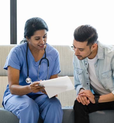 A clinician in scrubs with a stethoscope around her neck reviews paperwork with a patient.